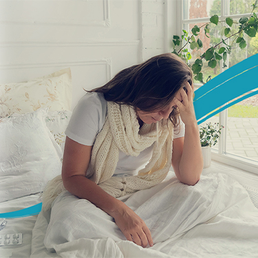 Hypothetical patient with anemia in beta thalassemia (BT) wearing a white shirt and pants, sitting next to the window with her hand on her forehead