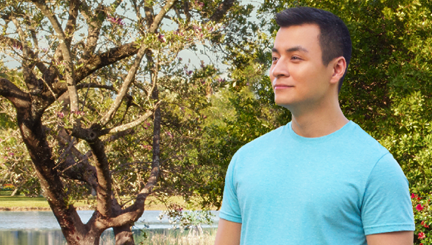Photo of a hypothetical patient in an aqua shirt outside near a lake in front of a tree with few leaves