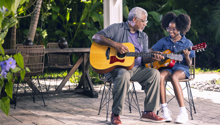 Photo of a hypothetical patient and loved one sitting outside, playing guitar together